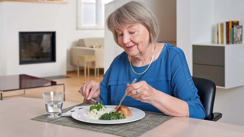 Eine Seniorin ist in ihrem Wohnzimmer am Essen
