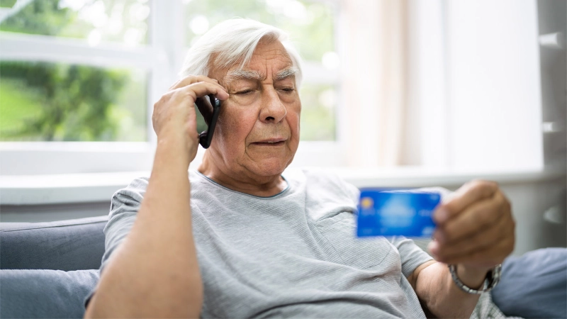 Un anziano è al telefono e contemporaneamente tiene in mano una carta di credito