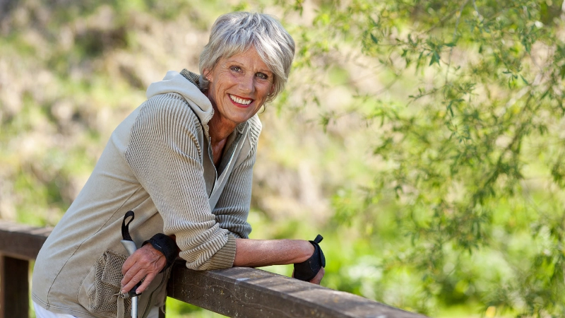 Eine Seniorin ist mit ihren Stöcken am Wandern und lächelt