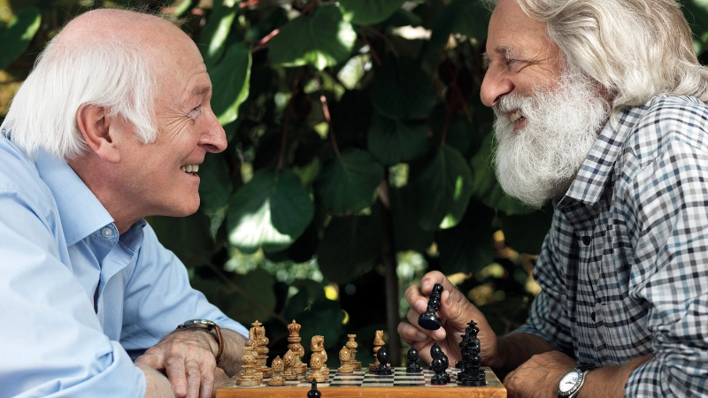 Deux seniors jouant aux échecs et riant ensemble.