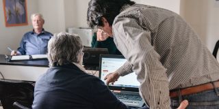Der Kursleiter steht gebeugt und zeigt dem Kursteilnehmer etwas im Laptop