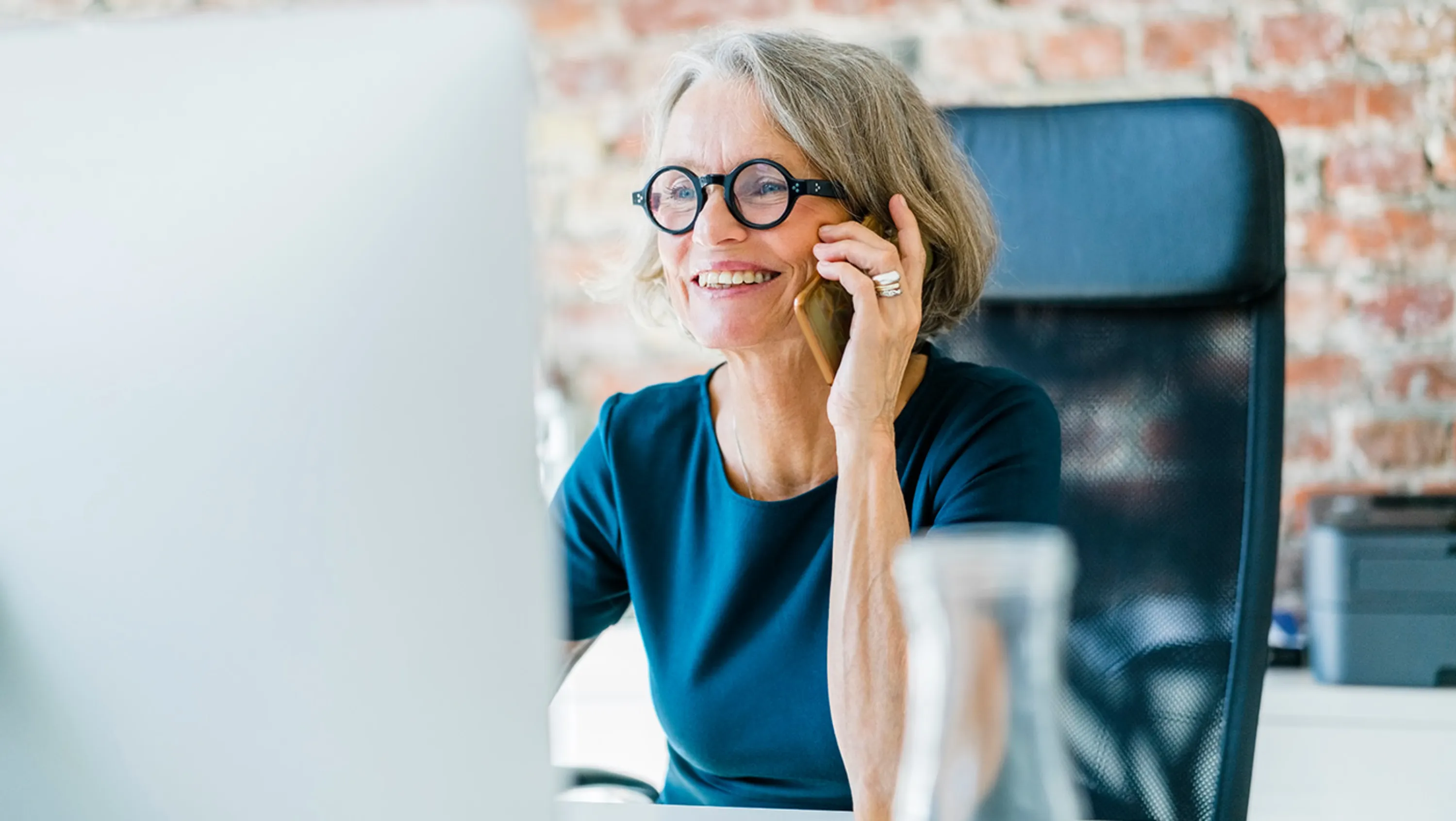 Frau am Telefon vor Bildschirm