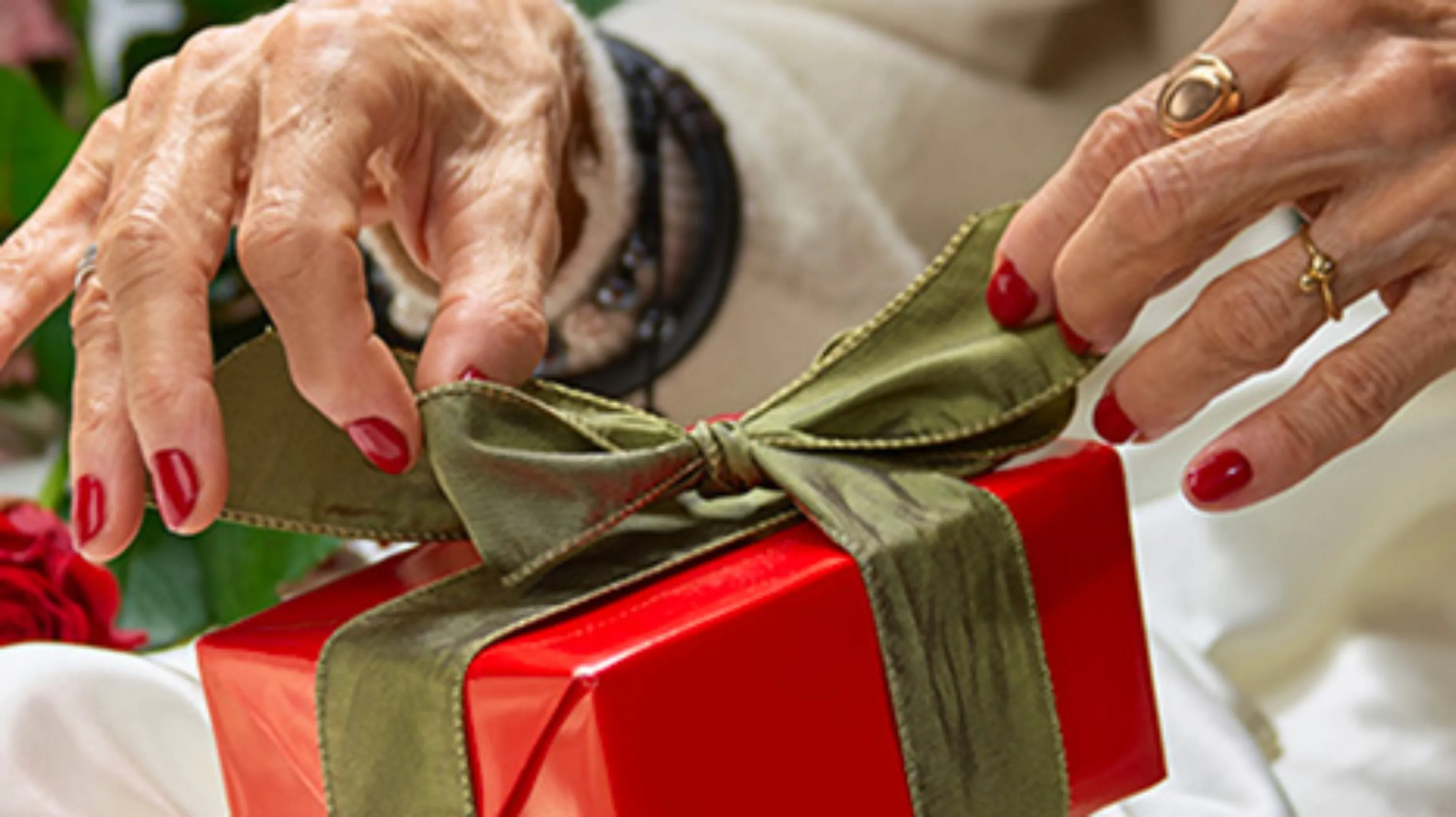 deux mains d'une personnes âgées détachent le ruban d'un cadeau