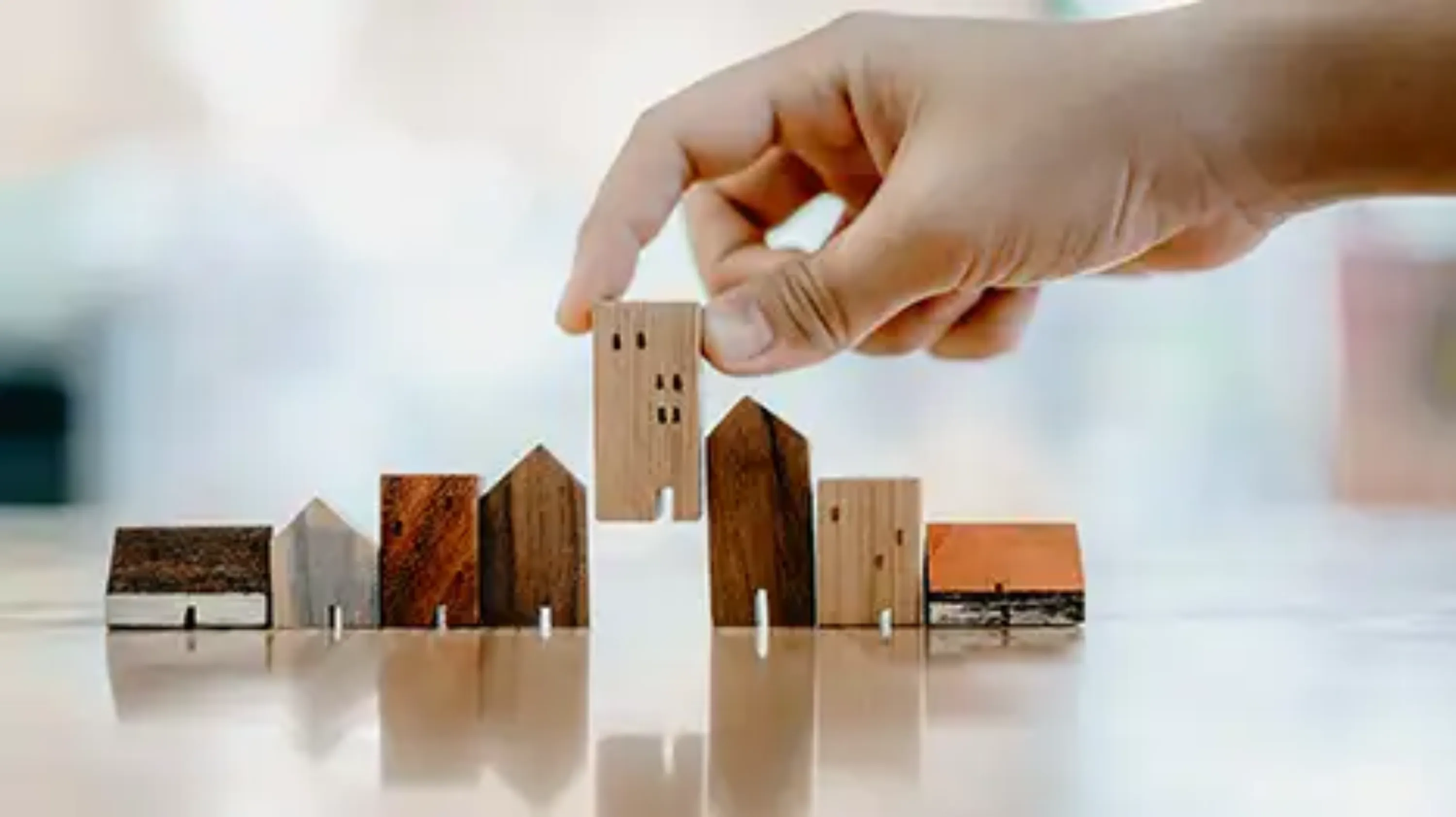 Main qui pose des maisons et des immeubles miniatures en bois sur un sol