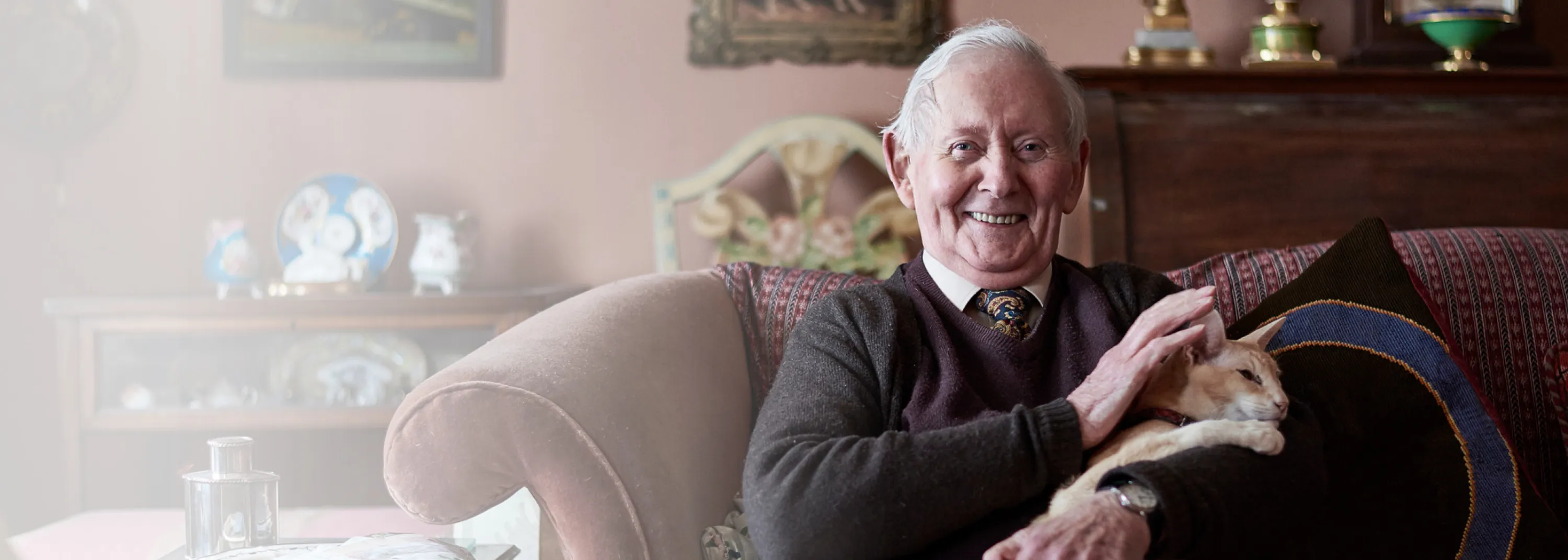 Ein älterer Herr sitzt mit Kate im Arm auf dem Sofa