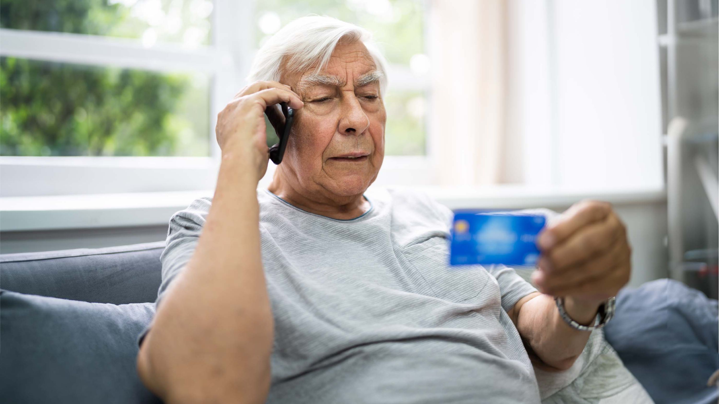 Ein älterer Herr ist am Telefon und schaut auf seine Kreditkarte.
