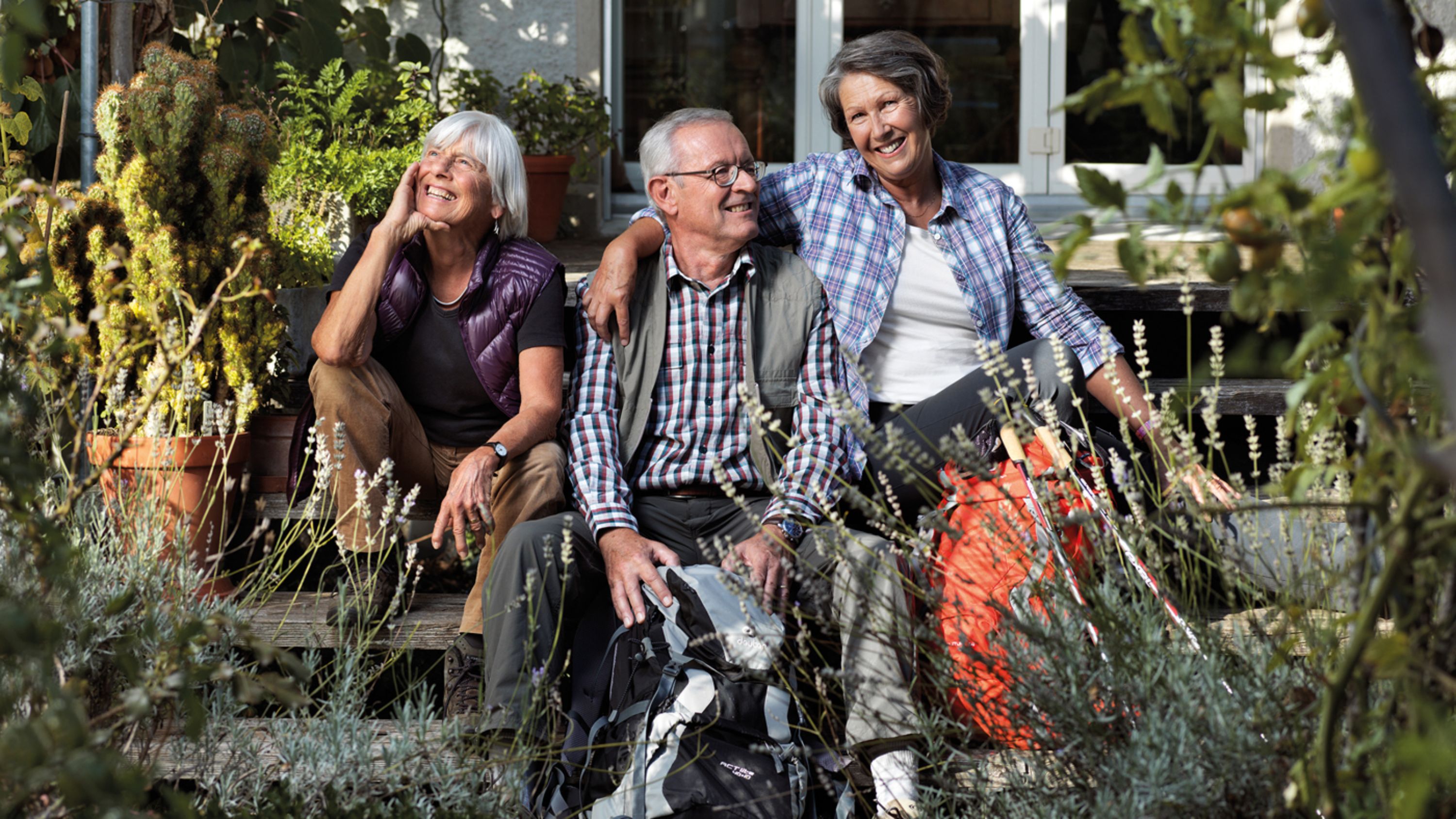 Trois personnes âgées sont assises sur les marches dans le jardin et rient.