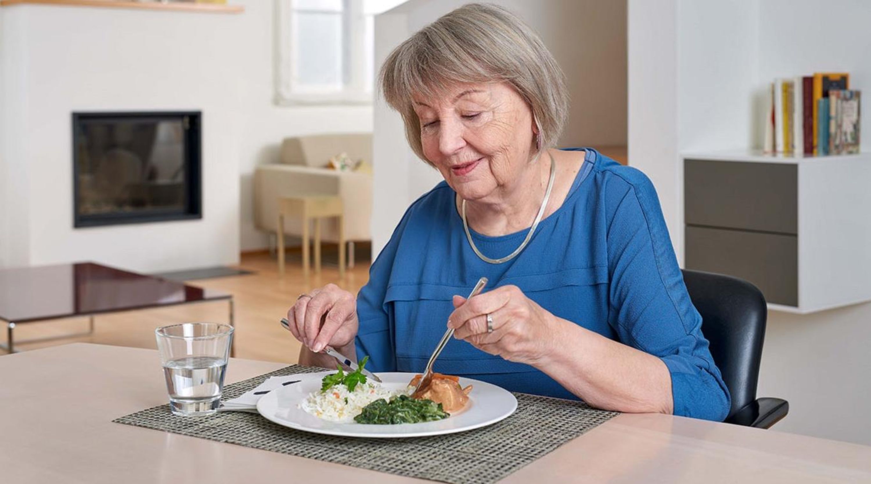 Seniorin isst ihre Mahlzeit am Tisch.