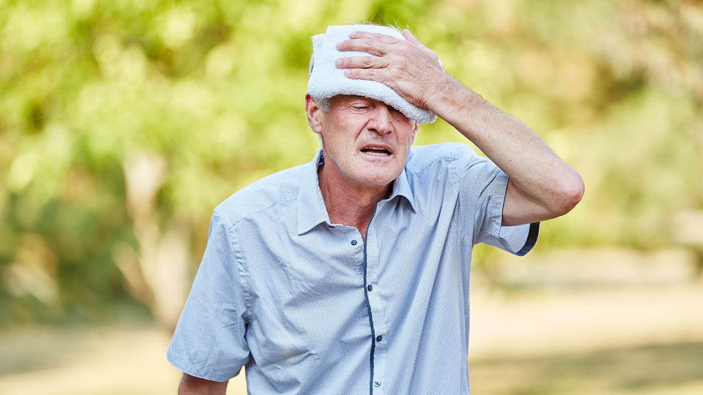 Ein Senior wischt sich seine Stirn mit einem nassen Lappen.