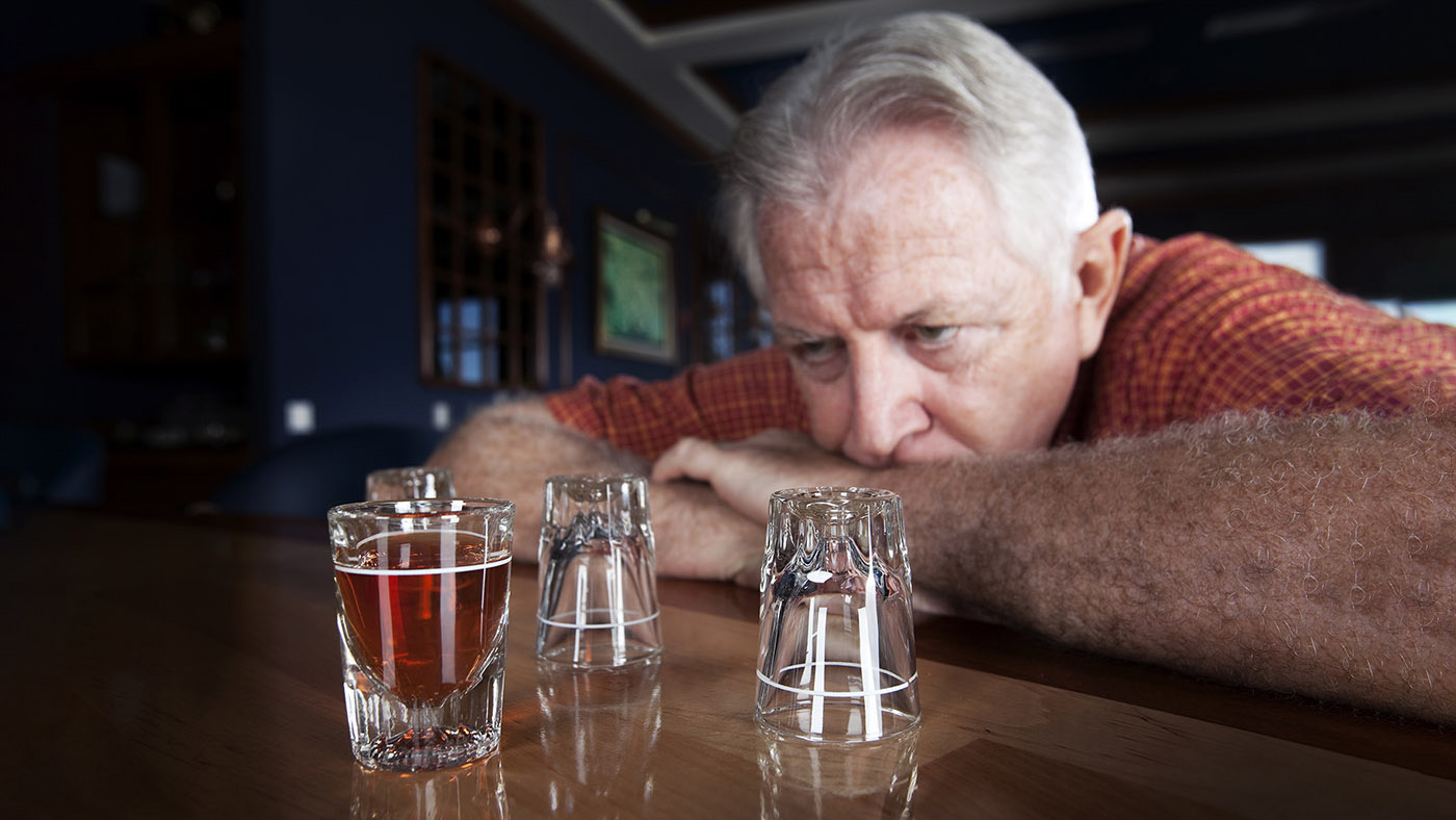 Un uomo anziano siede al bar e guarda bicchieri di alcolici vuoti e pieni.