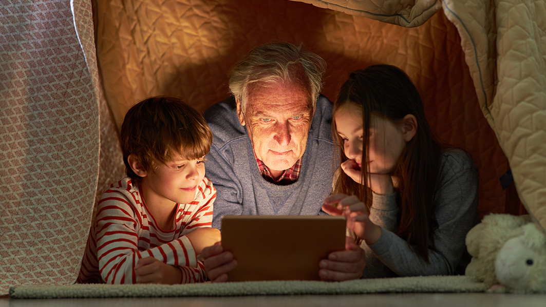 Ein Senior und seine beiden Enkelkinder schauen einen Film auf ihrem Tablet.