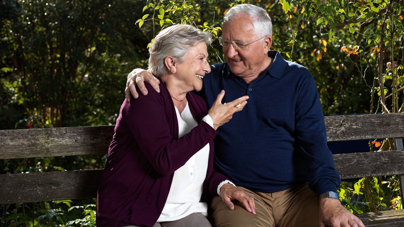 Una coppia di anziani è seduta felicemente su una panchina nel proprio giardino.