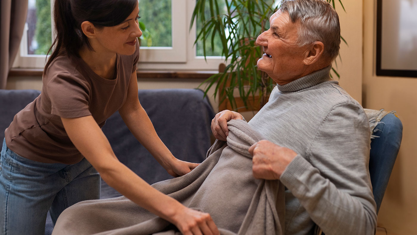 Une aide-soignante couvre un senior avec une couverture.